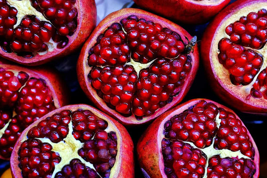 Flat lay of pomegranate-themed perfumes including Jo Malone Pomegranate Noir, Bvlgari Omnia Coral, Solinotes Grenade, Guerlain Granada Salvia, and other fruity-floral scents with pomegranate imagery.